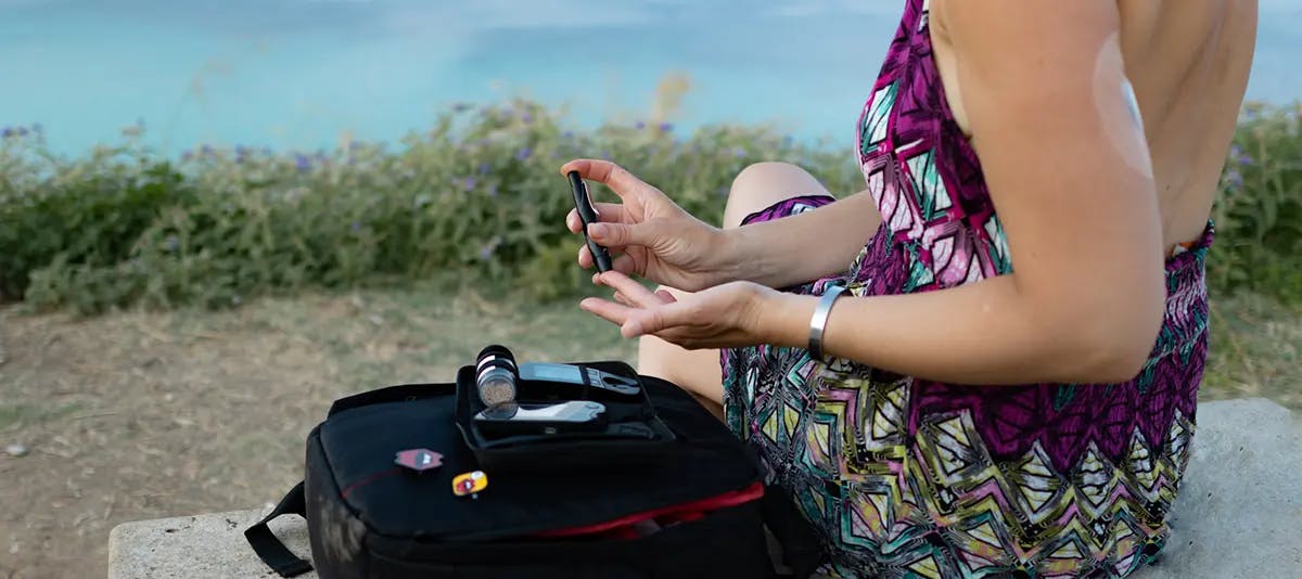 Dame misst ihren Blutzucker während sie auf einem Stein am Meer sitzt.